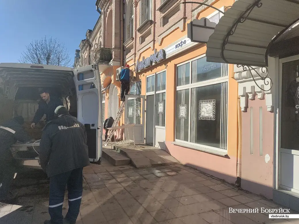 Бобруйск, улица Социалистическая, 15 марта 2022 года. Рабочие предприятия «Водоканал» выносят оборудование, снимают кондиционер возле вывески кафе «Лакомка».